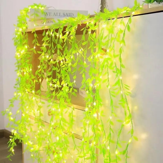 Awadhamrt Artificial green vines with string lights draped over a wooden shelf.