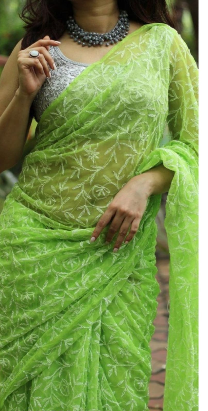 A woman showcasing a green and white georgette saree with Lucknow Chikankari and Tepchi hand embroidery work all over.